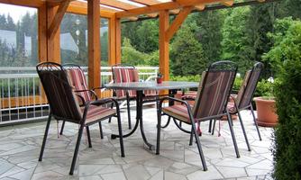 A cozy conservatory with a round table and six chairs. The room has a bright atmosphere and is surrounded by trees.