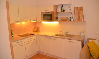 A modern kitchen with bright cabinets and warm lighting. It includes cooktops, a sink, and decorative accessories.