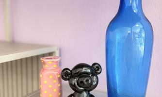 A colorful arrangement of decorative objects on a shelf. Below are a black bear figurine, a pink polka-dotted vase, and a blue glass bottle.