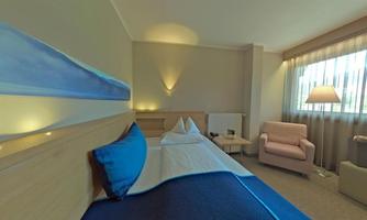 A modern room with a cozy bed and a comfortable armchair. The room features soft colors and plenty of natural light.