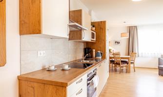 A modern kitchen with wood and white cabinets. In the background, there is a dining area with a table and chairs.