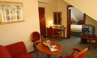 A cozy room with a red sofa and a round table. In the background, a bed and a desk with a mirror can be seen.