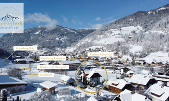 A picturesque winter village with snow-covered roofs and mountains in the background. In the foreground, a building is visible, surrounded by an idyllic landscape.