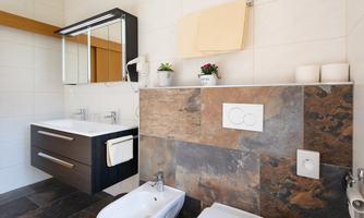 A modern bathroom with a double sink and a large mirror. The walls are tiled in light colors, and there are decorative plants on the sink.