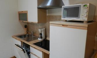 A modern kitchen with a dishwasher, a microwave, and a stainless steel production area. The walls are bright and the furniture has a light wood appearance.