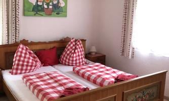 A cozy bedroom with a wooden bed and plaid pillows. On the wall, there is a picture of two funny characters.