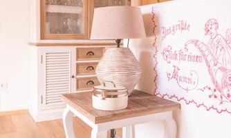 A cozy room with a wooden floor and a white dresser. On a table, there is a lamp, next to it a wall with red writing.