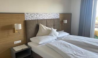 A modern bedroom with two single beds and elegant wooden decor. The room is bright and friendly, with windows that let in daylight.
