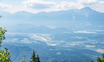 A wide landscape with mountains and a river, surrounded by gentle hills. The sky is clear with a few clouds.
