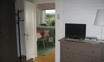 A simple room with a wardrobe and a dresser. Through the door, you can see an adjacent room with a table and chairs.