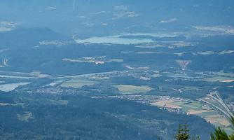 An impressive mountain landscape with green forests and blue mountains in the background. The sky is clear with some clouds.