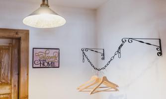 A cozy room with a lamp and coat hangers on a wall. On the wall hangs a sign that reads "Welcome to your Home".