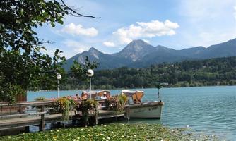 A calm lake with boats and a picturesque mountain backdrop. Surrounded by green plants and colorful flowers.