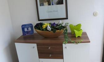 A modern sideboard with a wooden surface stands in a room.  
On top, there is a vase with flowers and a decorative element in the shape of a butterfly.