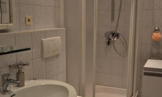 A modern bathroom with a shower, a sink, and a toilet. The walls are tiled, and the furnishings are in light colors.