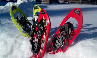 Three snowshoes in bright colors are standing in the snow. In the background, snow-covered hills and a serene landscape can be seen.
