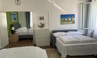 A bright bedroom with two beds and a mirror. The room has a colored wall and a beautiful picture on the wall.