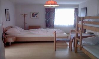 A simple room with a bed, a wooden living wall, and a bunk bed. There is plenty of daylight through the window and a cozy atmosphere.