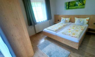 A cozy bedroom with a double bed and bright bed linen. Large windows bring daylight and a view of nature.