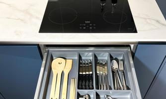 A modern kitchen with an open drawer that displays well-organized cutlery and cooking utensils. Above it is a cooktop and two bottles of oil.