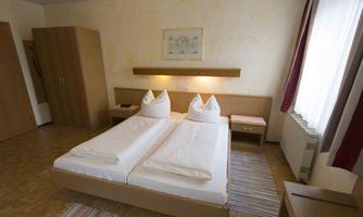A simple bedroom with two single beds and wooden furniture. The room has plenty of natural light and a cozy atmosphere.