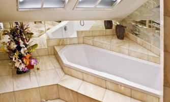 A modern bathroom with a white bathtub and elegant tiles. A floral arrangement adorns the space and large windows provide plenty of light.