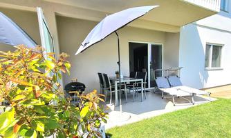 A cozy outdoor area with a table, chairs, and loungers. A sunshade provides shade, and the green lawn invites you to relax.