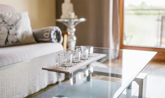 A stylish living room with a comfortable sofa and a glass coffee table. On the table, there are four candles in jars, surrounded by decorative stones.