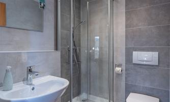 A modern bathroom with a glass shower and a sink. The walls are tiled in neutral gray tones.