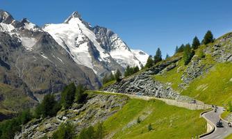 A picturesque mountain landscape with snow-covered peaks and green meadows. A winding path meanders through nature.