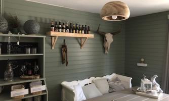 A cozy room with a wooden shelf holding bottles. A deer antler hangs on the wall, and a light sofa invites relaxation.