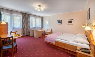 A bright hotel room with a double bed, a table, and chairs. Large windows provide plenty of natural light.