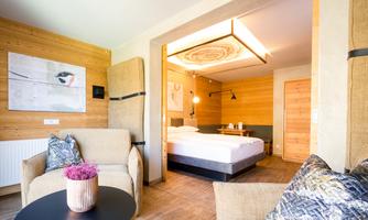 A stylish hotel room with wooden paneling, a comfortable bed, and cozy seating. Natural light streams through the window, creating an inviting atmosphere.