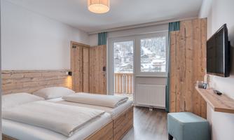 A cozy hotel room with two beds and wooden details. The room has a large window with a view of the mountains.