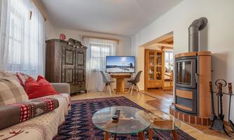A cozy living space with a sofa, a round table, and a modern fireplace. The room is bright and friendly, with a TV and a rustic cabinet.