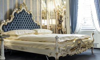 An elegant bedroom with an artistically adorned bed and luxurious bedding. Behind the bed is a mirrored wall with decorative elements.