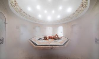 A luxurious room with a gentle steam bath and bright light. A person is lying relaxed on a marble block.