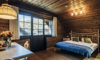 A cozy apartment with wooden ceilings and a large window. The room is equipped with a double bed and a dining table.