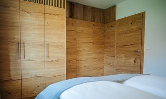 A modern bedroom area with wooden cabinets and a simple bed. The warm wood tones create an inviting atmosphere.