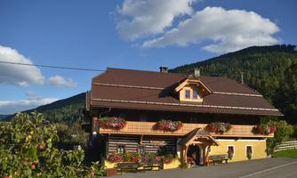 A picturesque little house in the mountains with blooming flowers at the windows. In the background, green hills and a blue sky can be seen.