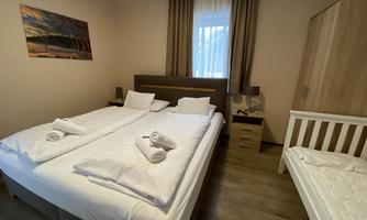 A bright bedroom with two beds and towels on the bedding. A child's bed is also available, and there is a window to let in light.