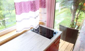 A modern kitchen with a ceramic glass cooktop and a window view into nature. The white curtains with purple stripes create a bright and friendly atmosphere.