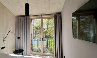 A modern bedroom with large windows overlooking a garden. The walls are light and the furnishings are simple and elegant.
