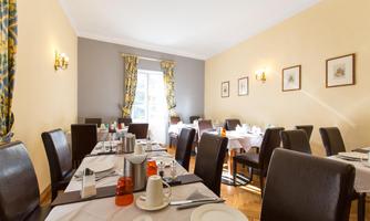 A bright dining room with set tables. The walls are painted in soft colors and there are windows with curtains.