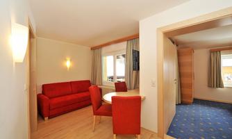 A bright living room with a red sofa and a table. The room has large windows and a modern style.