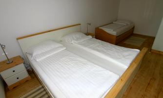 A simple bedroom with two single beds and an additional bed. The room is bright and minimalist with wooden flooring and nightstands.