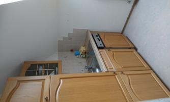A small kitchen with wooden cabinets and a sink. The walls are bright, and there is space for kitchen appliances.
