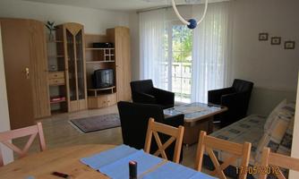 A cozy living room with a dining area, black armchairs, and a television. Large windows provide plenty of daylight.