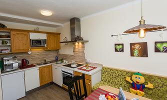 A cozy kitchen with wooden cabinets and modern appliances. On the table are fresh fruit and a funny stuffed animal.