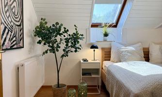 A cozy bedroom with a wooden bed and bright pillows. A plant and decorative glass containers create an inviting atmosphere.